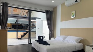Habitación de hotel moderna con una cama grande, una mesita de noche, aire acondicionado de pared y vistas a la cocina y el comedor a través de una puerta de cristal.