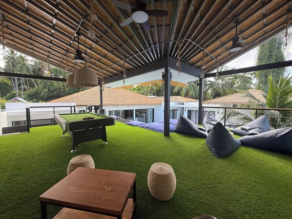 An outdoor lounge area with artificial grass, a pool table, and comfortable seating.