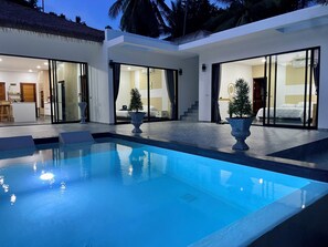 A modern house with a swimming pool, large glass doors leading to a bedroom, and a dining area.