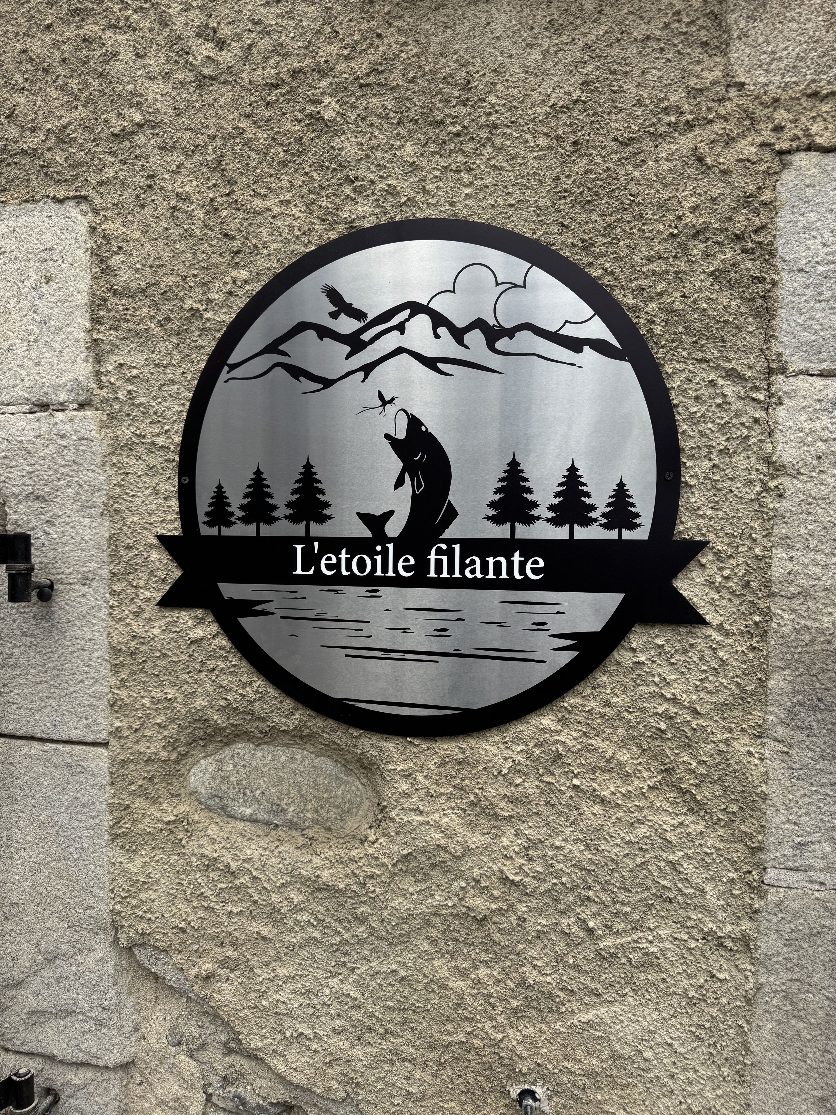 A circular sign with a silhouette of a person fishing, trees, and mountains.