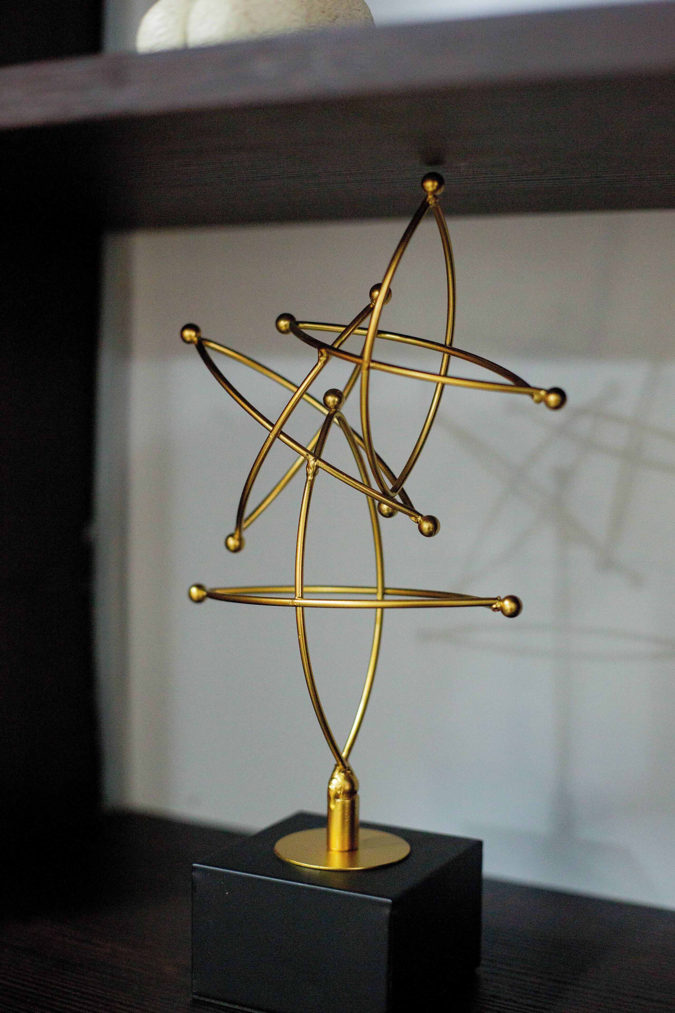 Escultura metálica geométrica sobre uma base preta.