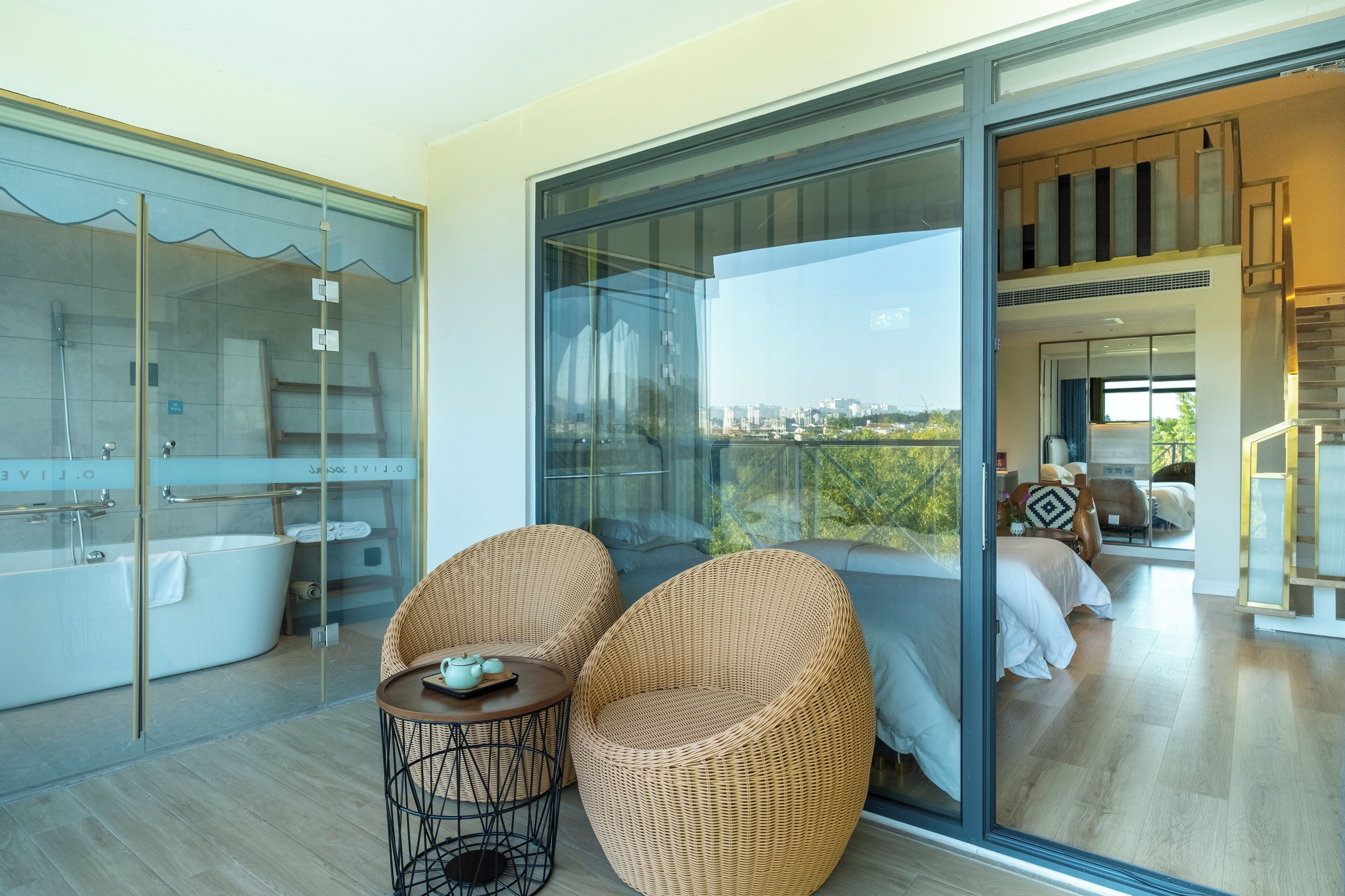 A modern bathroom with a glass-enclosed shower and a bathtub. There is a wicker chair and a small table with a teapot.