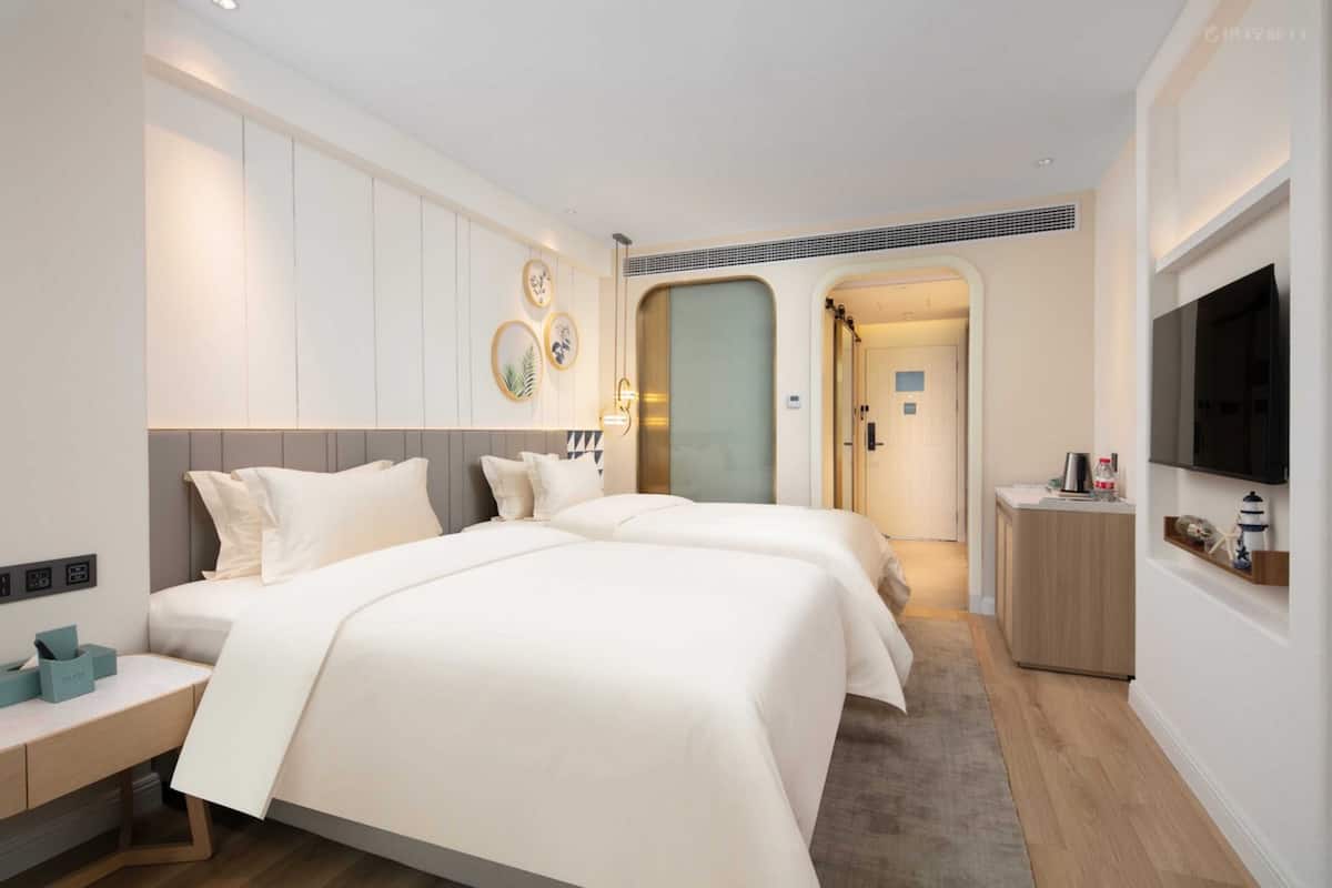 Quarto de hotel com uma cama grande, mesas de cabeceira, televisão e um banheiro visível através de um arco.