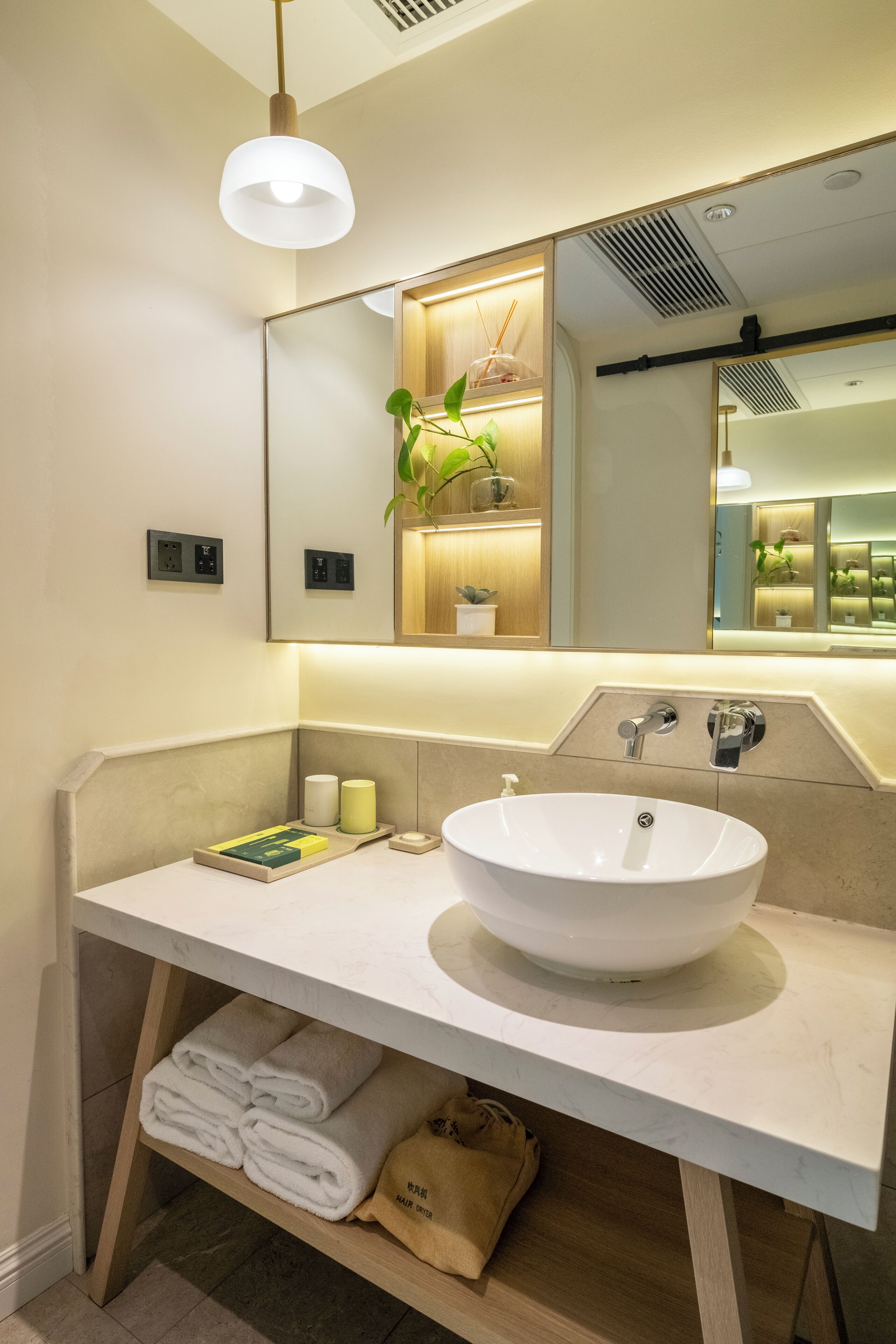 Un bany modern amb un lavabo blanc, un mirall i llums penjants. Hi ha tovalloles i productes de tocador al taulell.