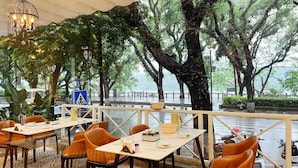 An outdoor dining area with tables and chairs, a hanging light fixture, and a view of a tree-lined street. - Guilin O-LIVE Social Hotel  (Guilin)