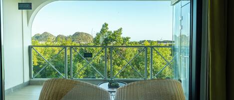 A balcony with wicker chairs and a table, overlooking a scenic view of trees and hills.