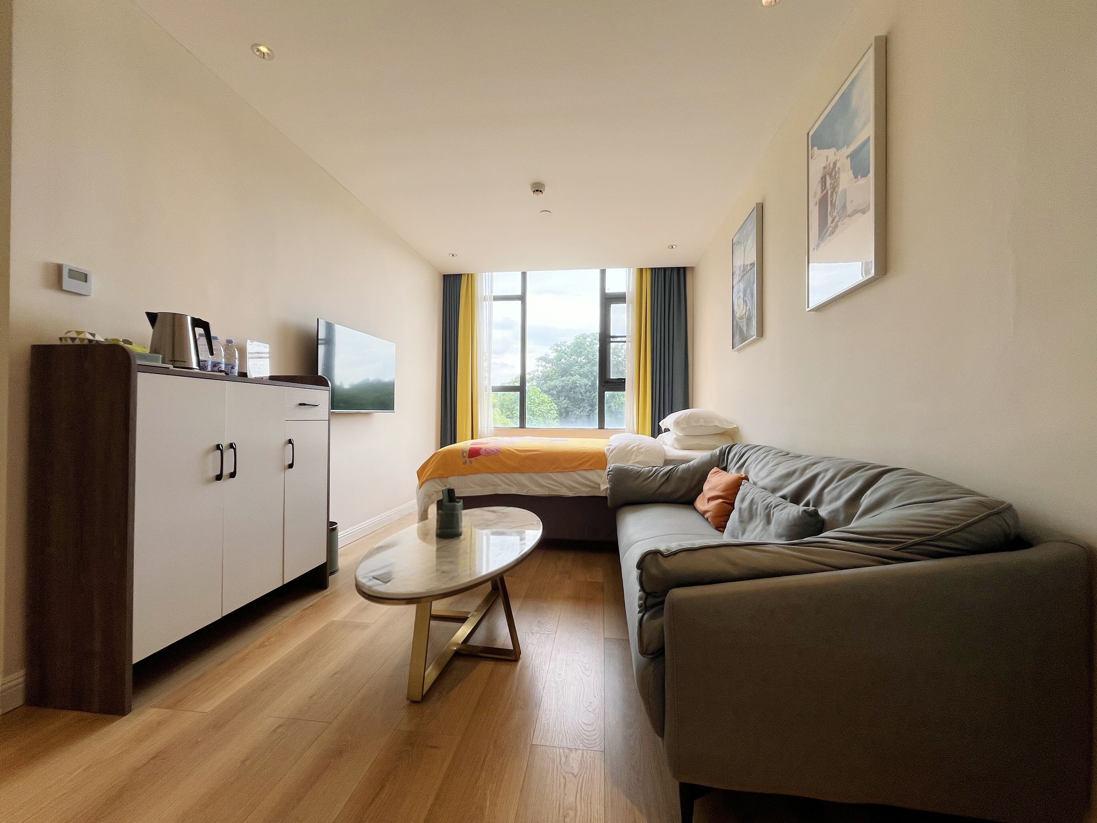 A modern hotel room with a sofa, a small table, a cabinet, and a bed.