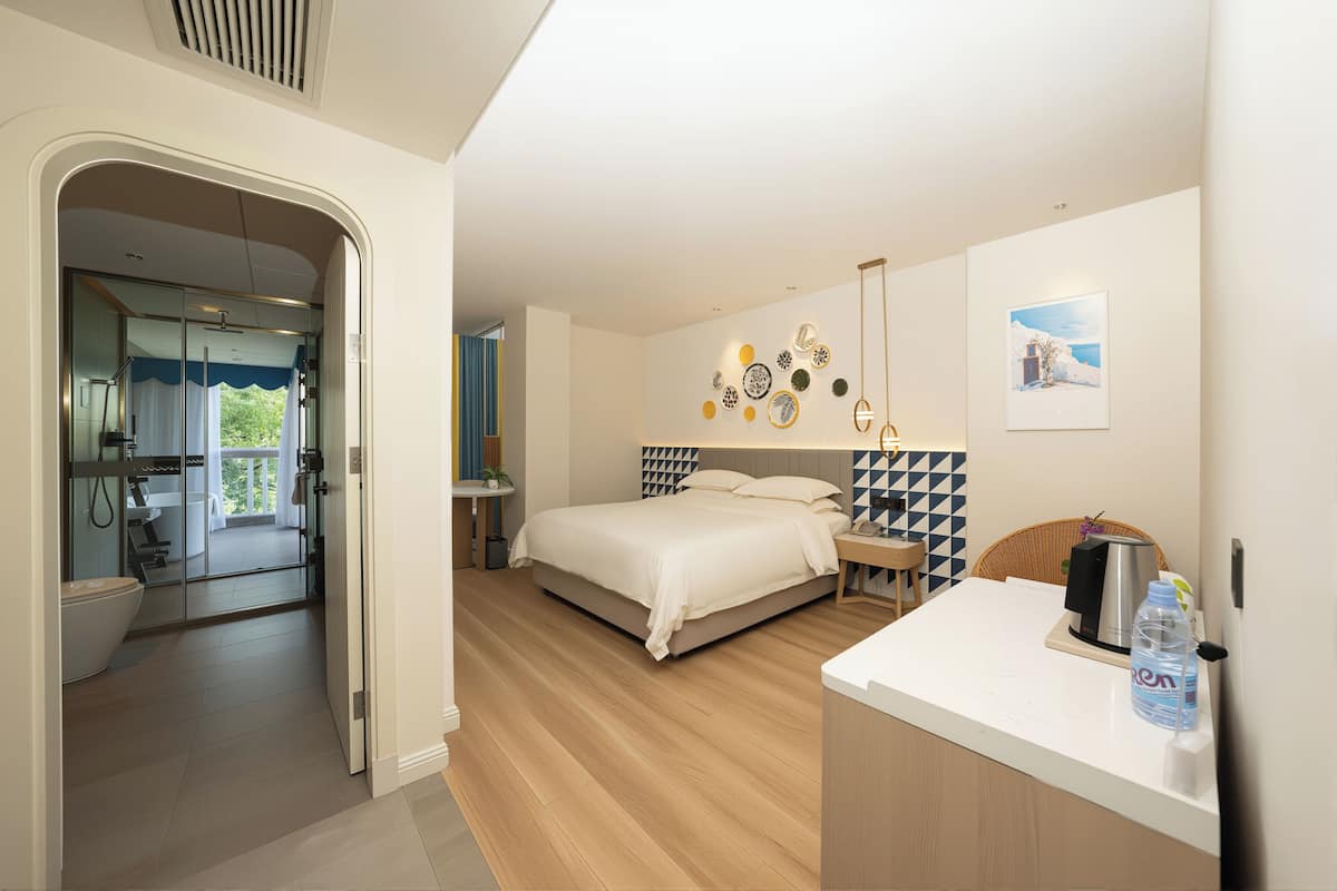 Quarto moderno com uma cama grande, uma mesa de cabeceira com chaleira e vista para a varanda.