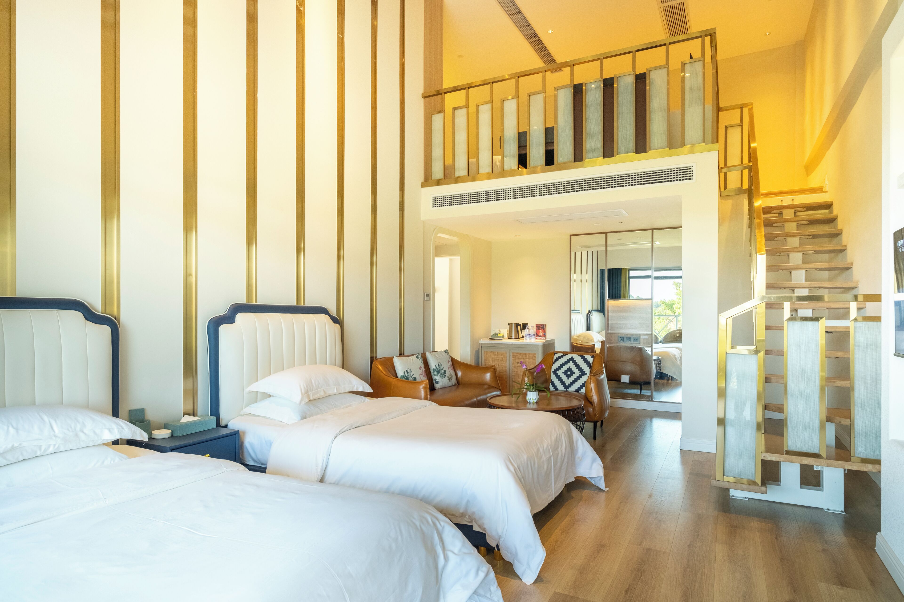 A hotel room with two beds, a sofa, a staircase, and a view of the outdoors.
