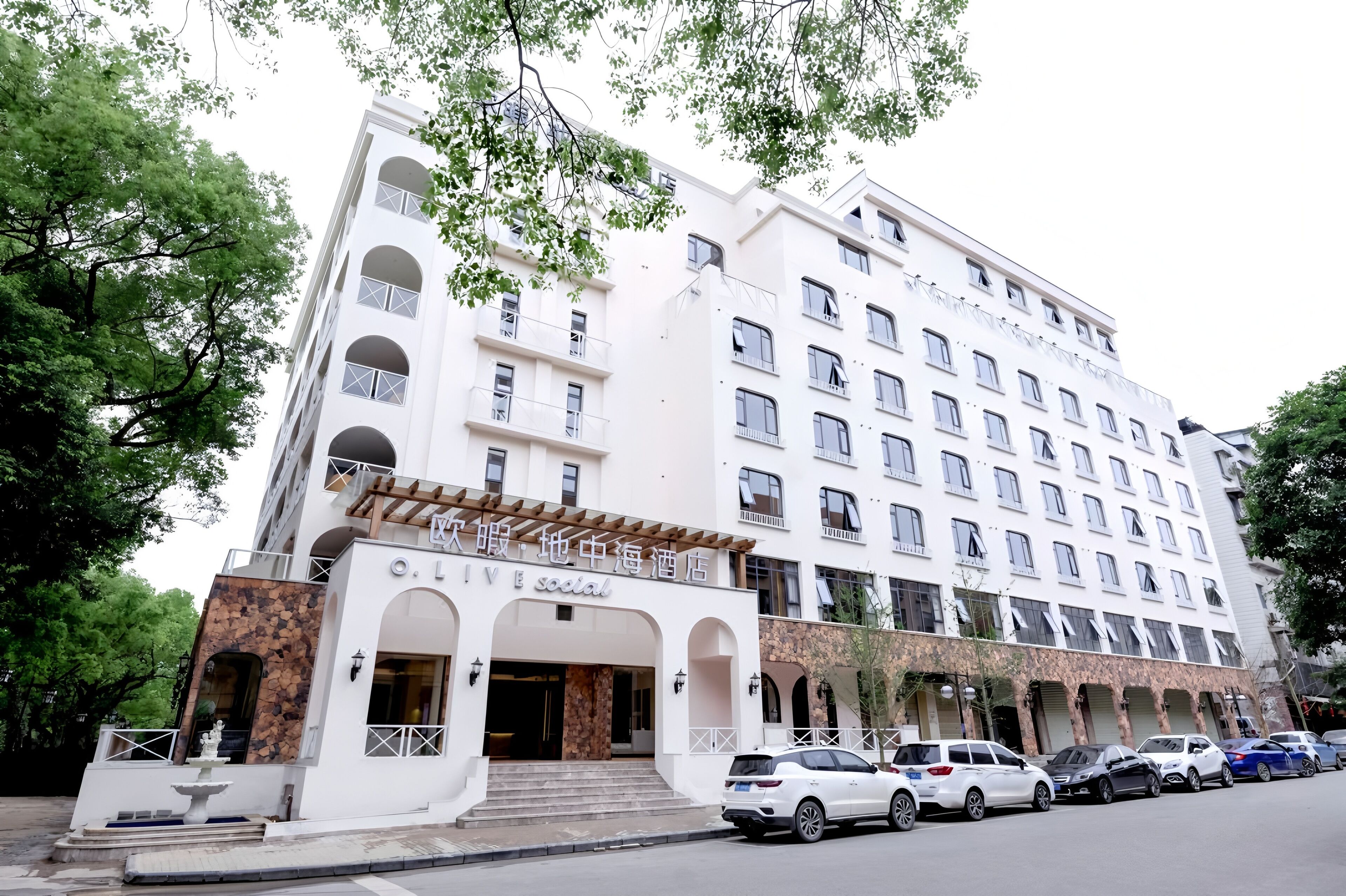 Un hôtel à plusieurs étages, doté d’une façade blanche, de nombreux balcons et d’un mur en pierre décoratif à l’entrée.