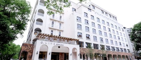 Un hôtel à plusieurs étages, doté d’une façade blanche, de nombreux balcons et d’un mur en pierre décoratif à l’entrée.