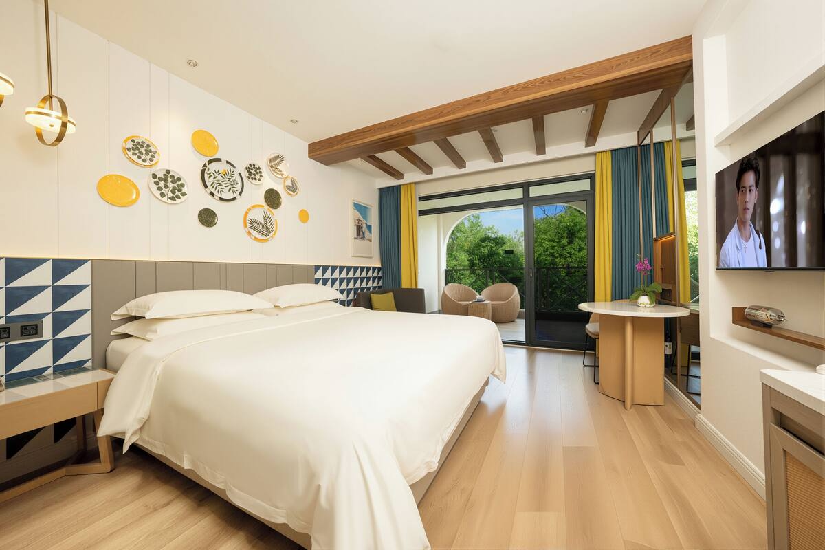 Quarto de hotel moderno com uma cama grande, uma escrivaninha, uma TV e vista para o exterior.