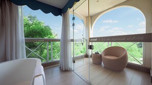 A balcony with a wicker chair, a white sofa, and a glass door leading to a lush green landscape. - Guilin O-LIVE Social Hotel  (Guilin)