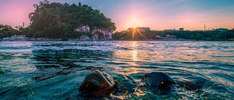A river with clear water, rocks in the foreground, and a sunset in the background.