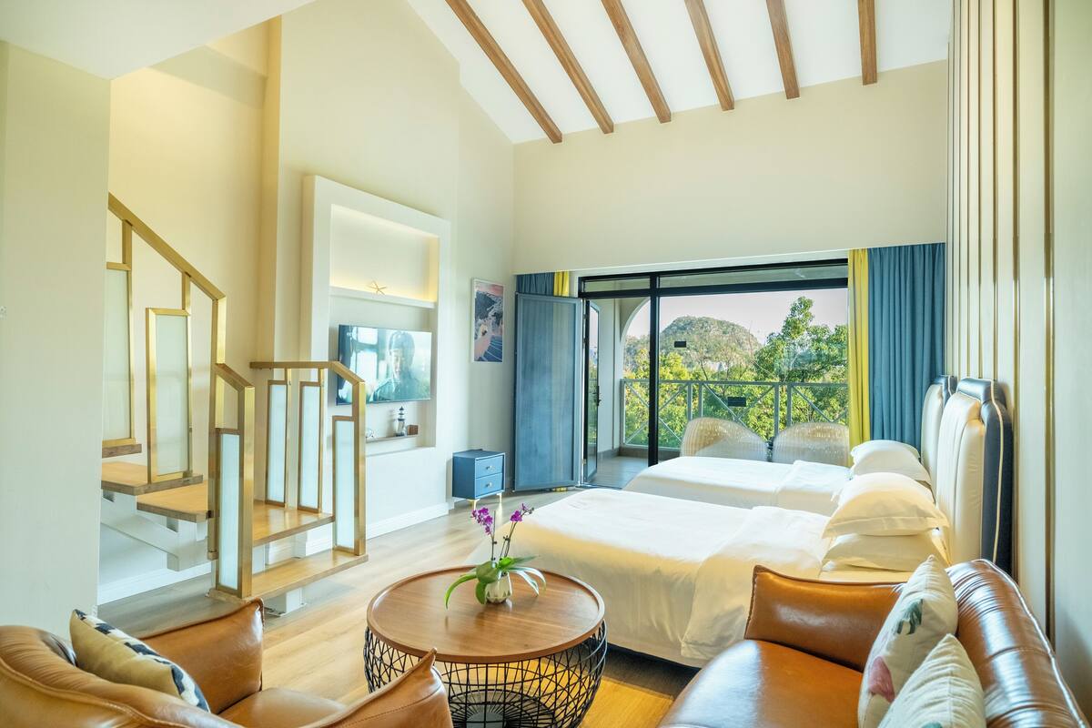 Quarto de hotel com cama, sofá, mesa de centro e escada.