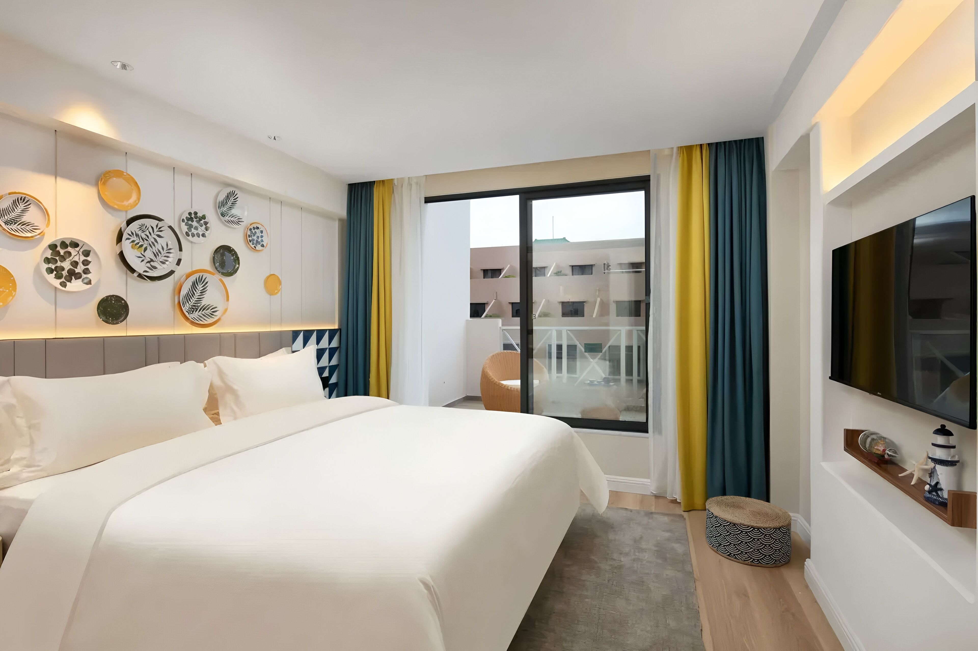 Una habitació d'hotel amb un llit gran, televisió, un balcó amb cortines i plats decoratius a la paret.