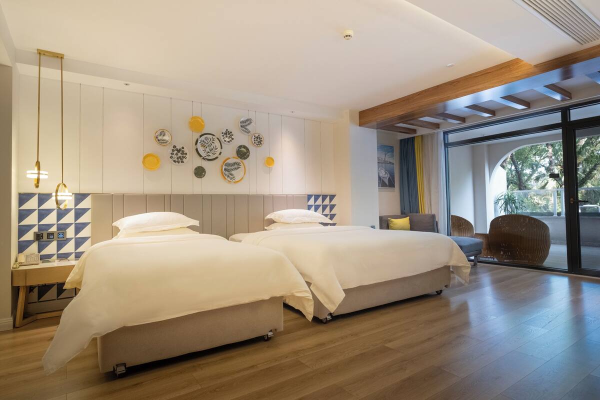 Quarto moderno com duas camas, piso de madeira, parede decorada com pratos e uma grande janela com vista para árvores.