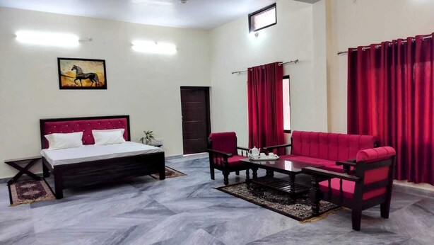 A hotel room with a bed, a red sofa, a coffee table, and a small table with a teapot. - Moonvilla Banquet And Hotels (Phulpur)