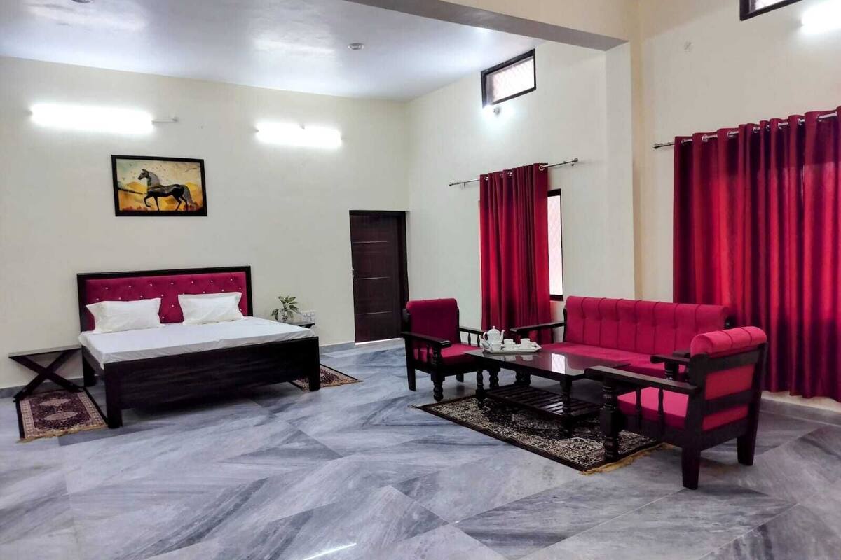 A hotel room with a bed, a red sofa, a coffee table, and a small table with a teapot.