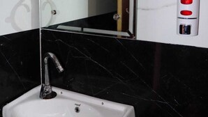 A bathroom with a white sink, a mirror, and a soap dispenser on the wall. - Moonvilla Banquet And Hotels (Phulpur)
