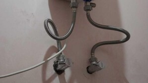 A white water heater mounted on a wall with two visible water supply connections. - Moonvilla Banquet And Hotels (Phulpur)