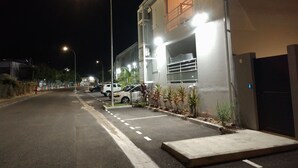 Ein Parkplatz neben einem Gebäude mit einem verschlossenen Eingang, Straßenlaternen und abgestellten Autos.