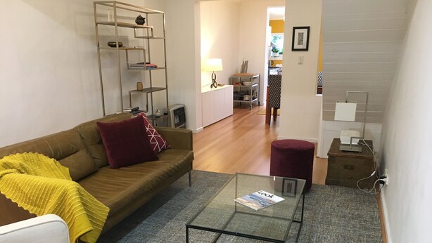 A living room with a glass coffee table, a brown sofa, a yellow blanket, and a red cushion. - Modern terrace home in inner Sydney (Saint Peters)