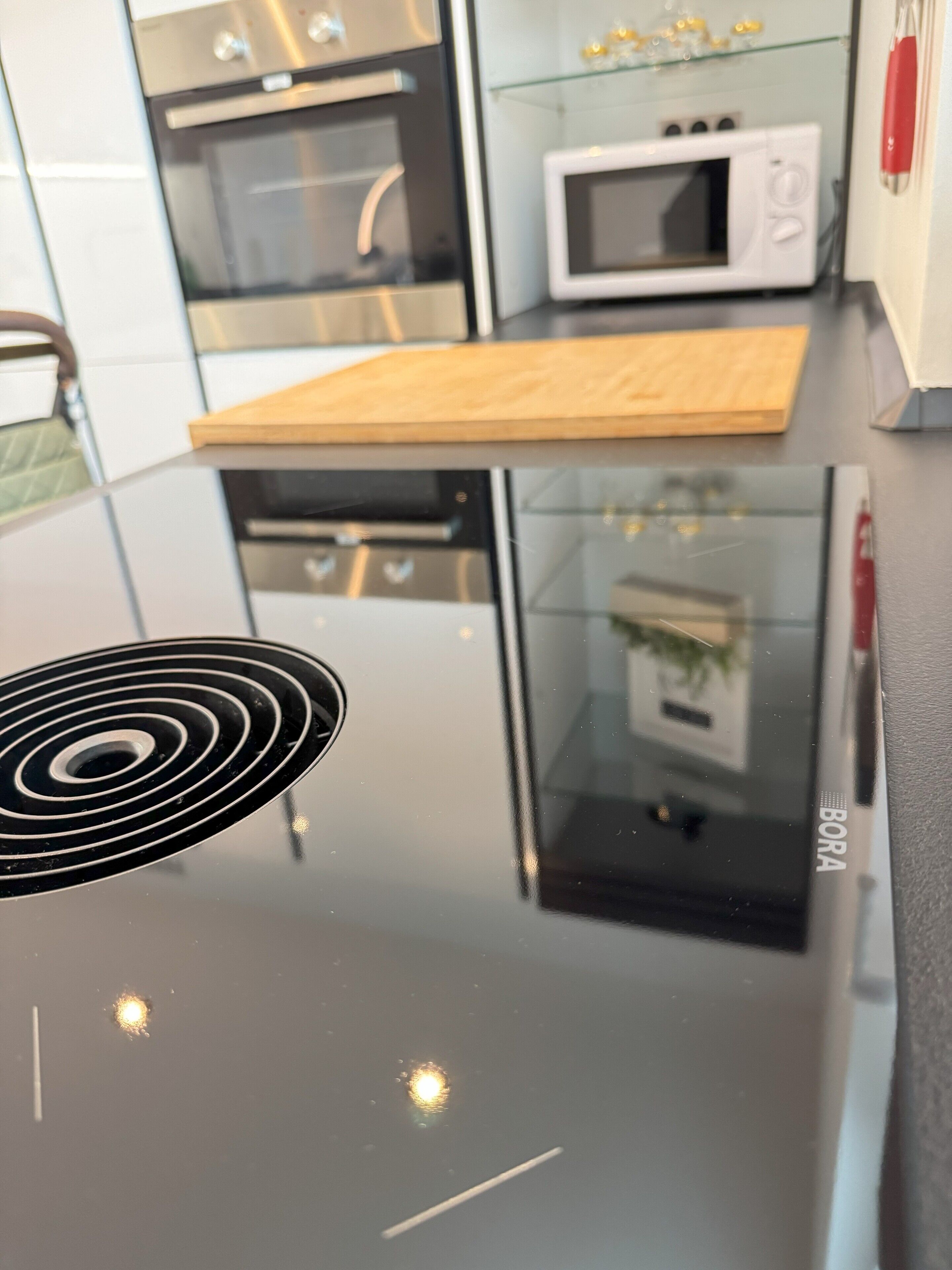 Une cuisine équipée d’une plaque de cuisson à induction noire, d’un four à micro-ondes et d’appareils électroménagers en acier inoxydable.