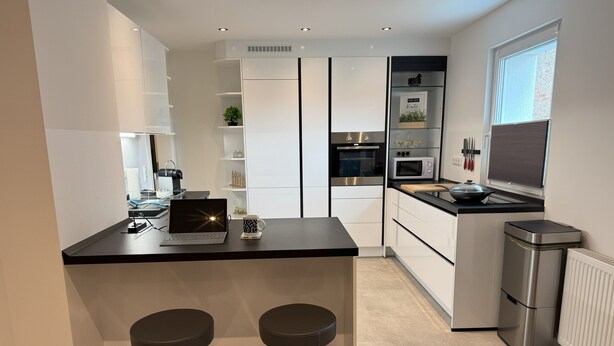 Een moderne keuken met een centraal eiland, barstoelen, een magnetron en een prullenbak.