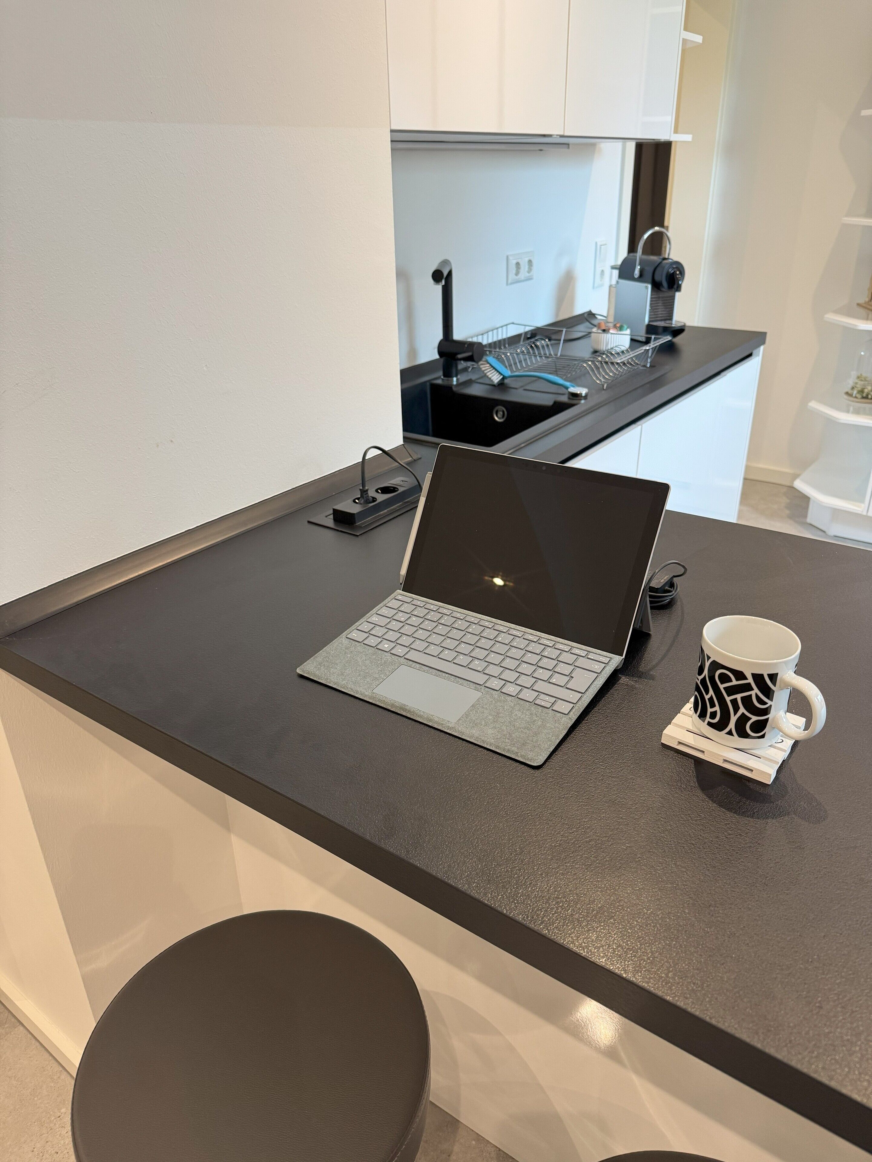 A modern kitchen with a laptop on a countertop, a mug, and a coffee machine.
