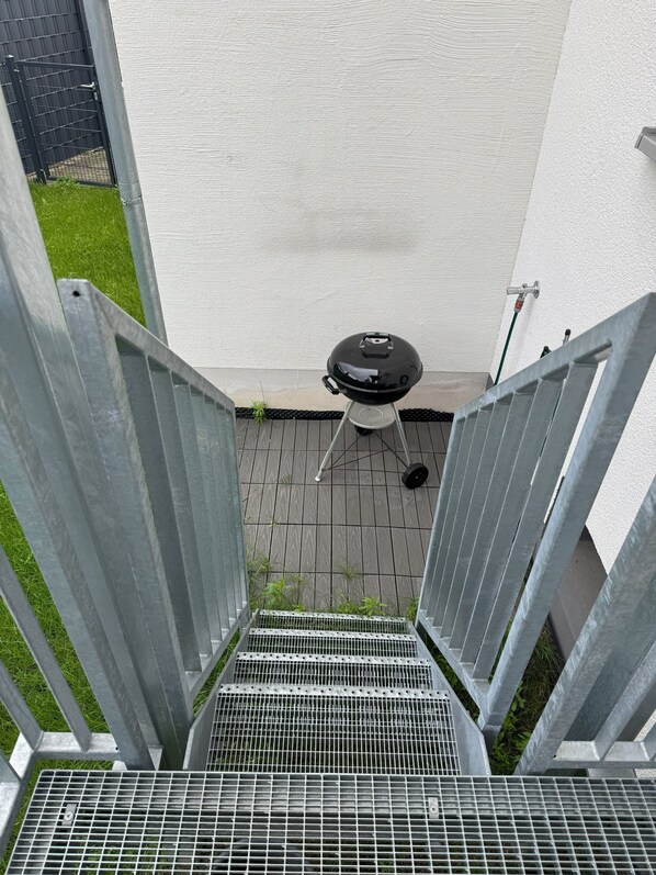 Un escalier en métal mène à un patio équipé d’un barbecue et d’un robinet d’eau.