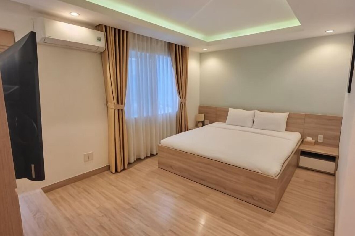 Une chambre d’hôtel moderne avec un grand lit, une tête de lit en bois, des tables de chevet et un appareil de climatisation.