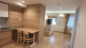 A modern kitchen with wooden cabinets, a dining area with a table and chairs, and a small TV mounted on the wall. - Simmi 4 Hotel & Apartment Near SECC (Ho Chi Minh City)