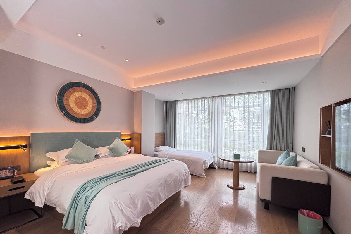 Una habitación de hotel moderna con una cama grande, una cama adicional, un sofá y una mesa redonda.
