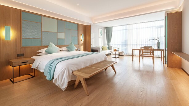 A modern hotel room with a large bed, a wooden bench, a desk, and a view of the city through large windows. - SSAW Boutique Hotel ZHIJIANG IMPRESSION (Hangzhou)