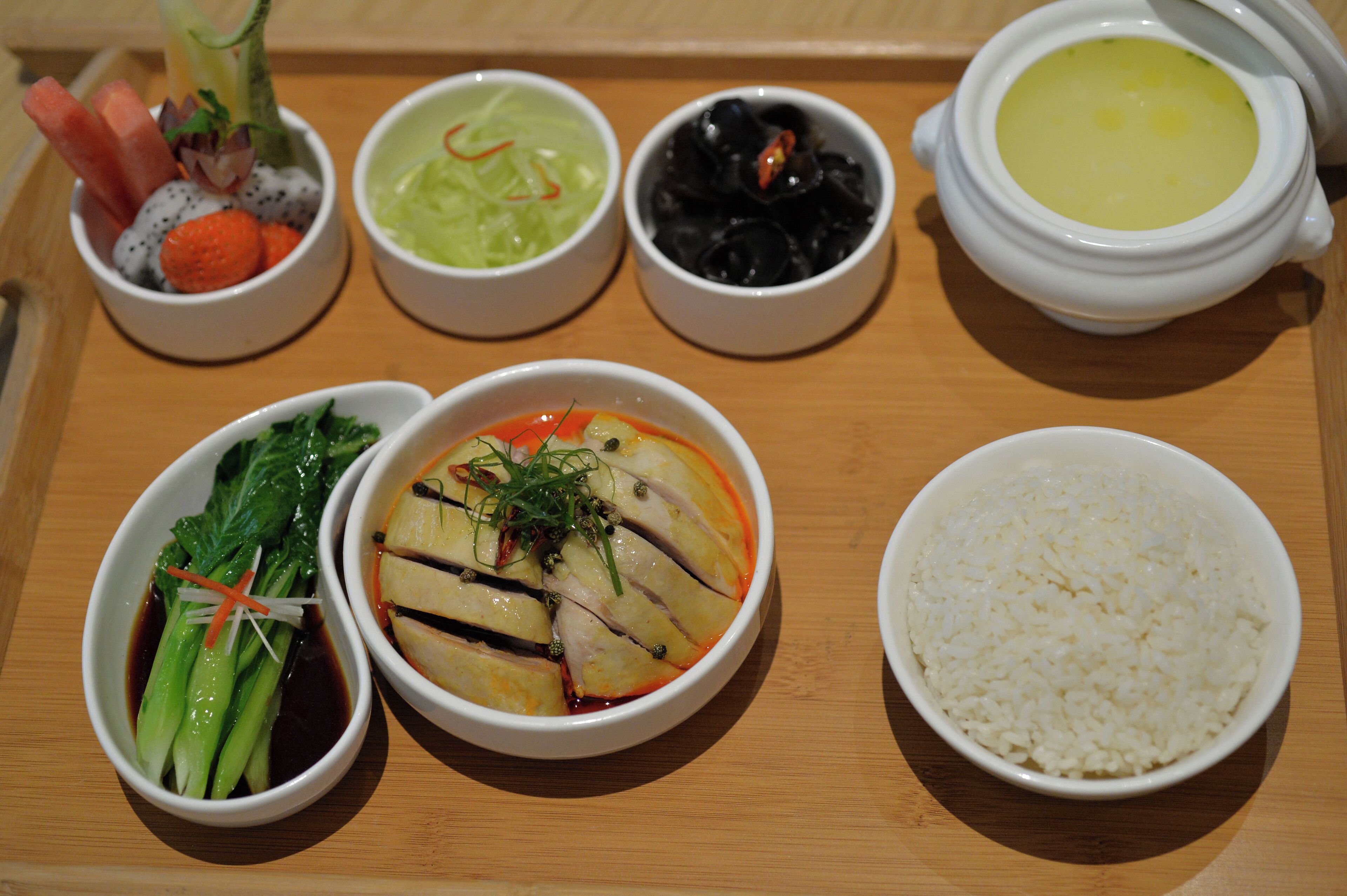 A wooden tray with various dishes including a bowl of rice, a bowl of soup, and several small bowls containing different foods.