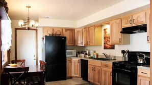 A kitchen with wooden cabinets, a black refrigerator, a stove, and a dining area with chairs and a table. - Cabin with Foosball-Southern Comfort (Big Bear Lake)