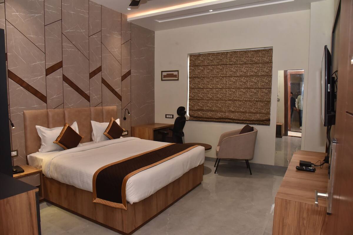 A modern hotel room with a large bed, a desk, a chair, and a TV.