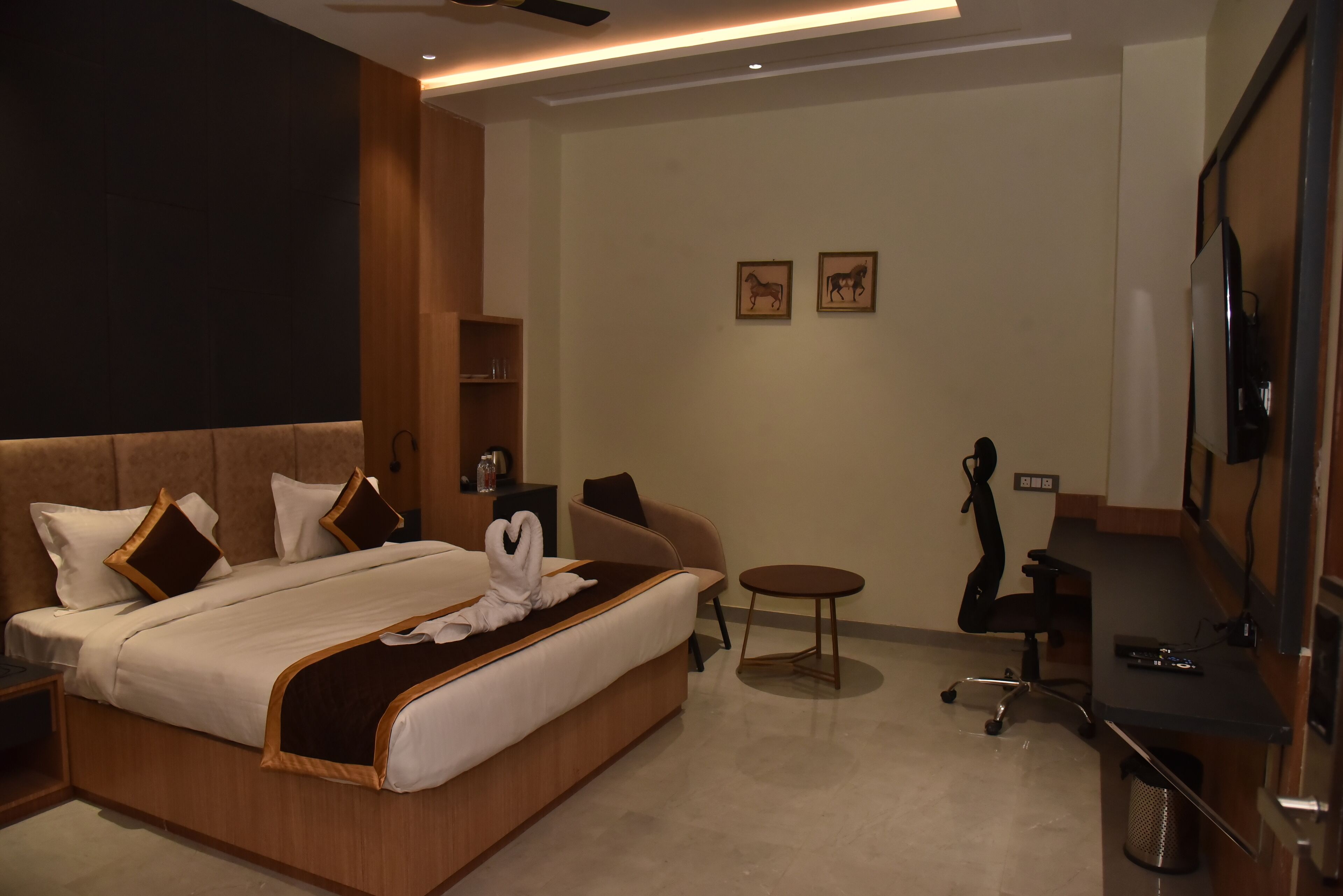 A modern hotel room with a large bed, a desk, a chair, a small table, and a TV.