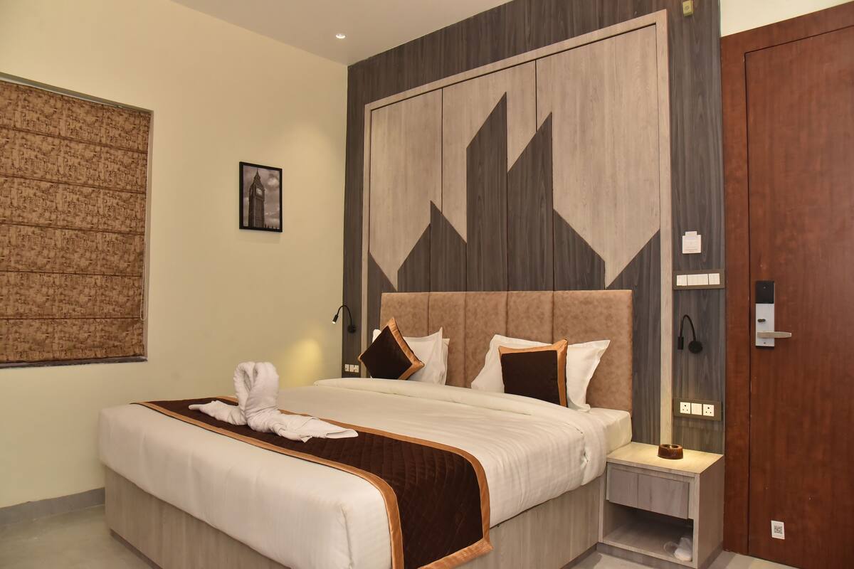 A neatly arranged hotel room with a large bed, a bedside table, a wall-mounted artwork, and a wooden door.