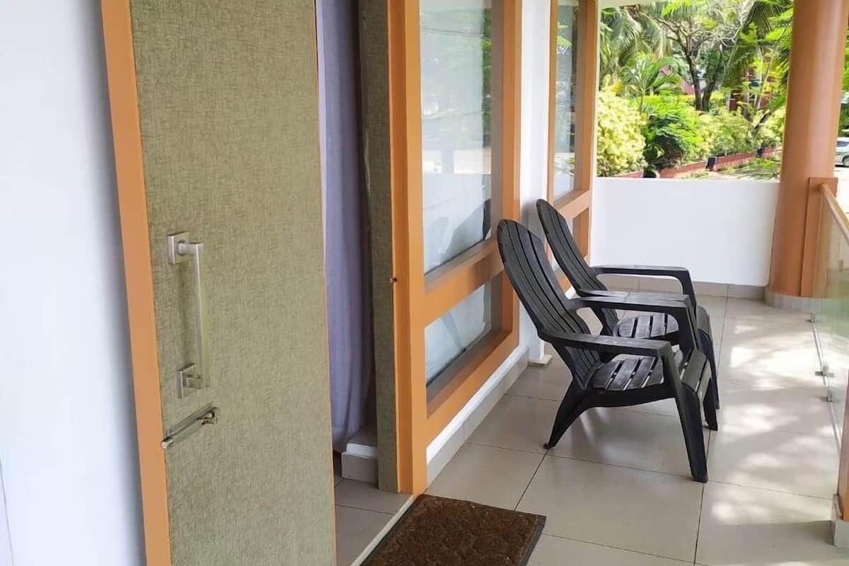 Eine offene Schiebetür führt zu einem Balkon mit Blick auf Grünflächen, zwei schwarze Plastikstühle und eine kleine Matte auf dem Boden.