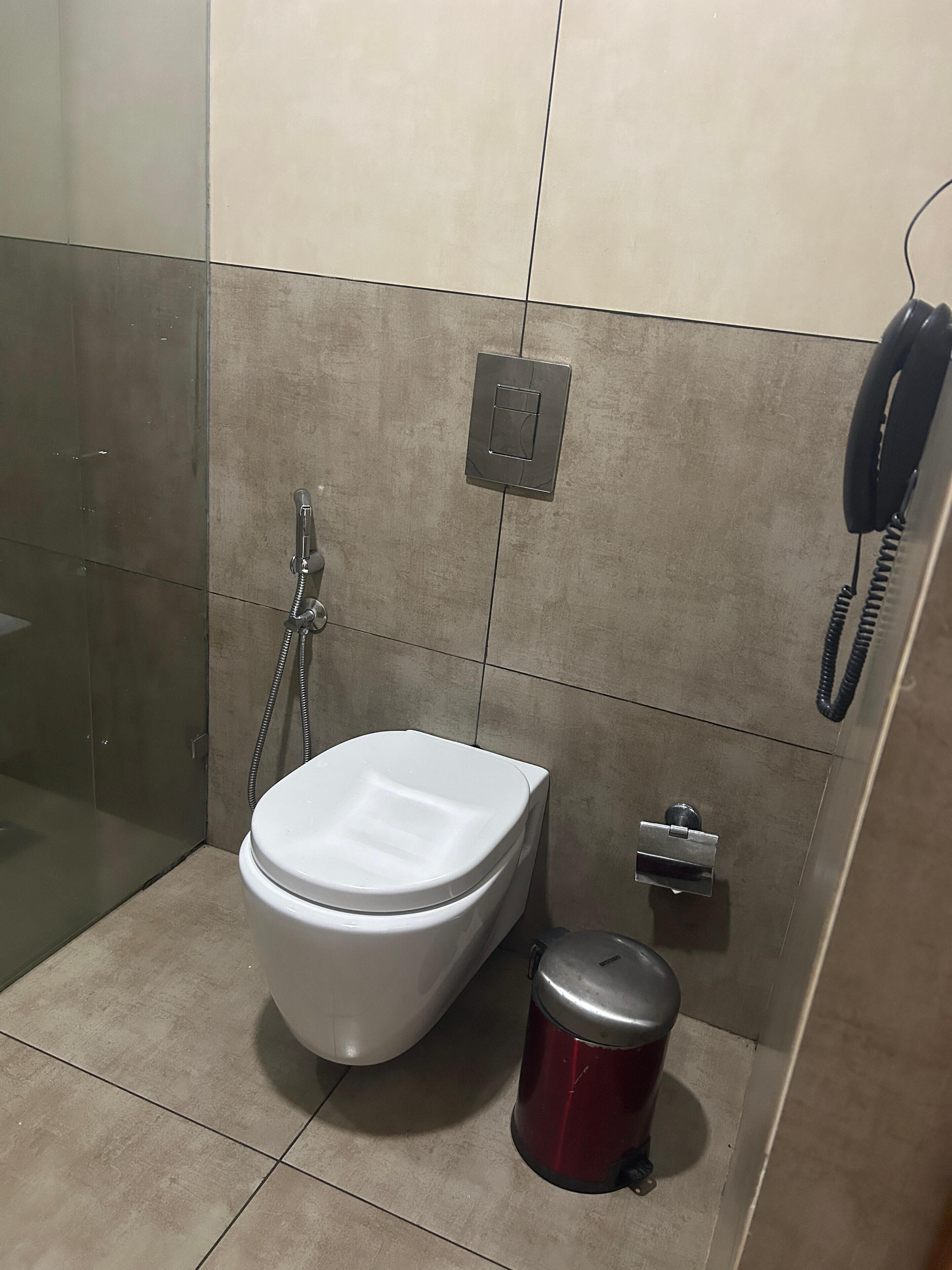 Uma casa de banho com sanita, um lixo, chuveiro e telefone.