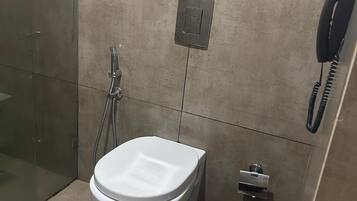 Uma casa de banho com sanita, um lixo, chuveiro e telefone.