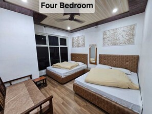 A four-bedroom accommodation with two single beds and two double beds, wooden flooring, and a ceiling fan. - Chauhan Annexe (Barkot)