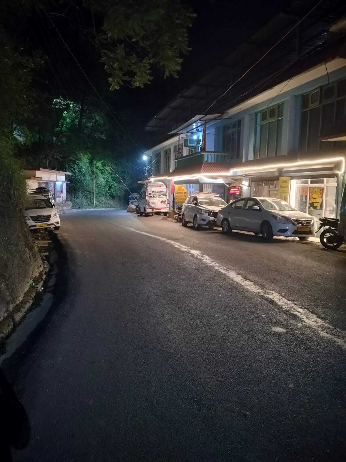 Vista de una calle por la noche, con un edificio que muestra un letrero que indica que es un hotel. Se ven varios coches estacionados y una furgoneta en la calle.