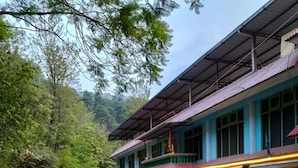 Un bâtiment avec une enseigne indiquant un hôtel et un restaurant, un espace extérieur abrité avec des tables, et une route qui tourne vers la gauche.