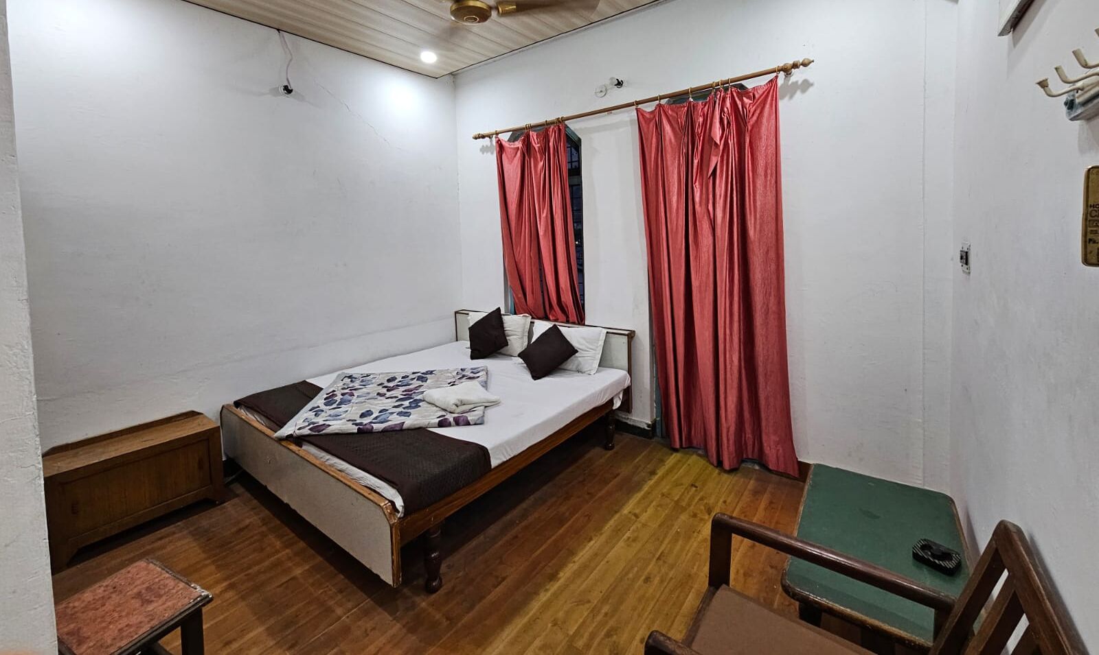 Una habitación pequeña y sencilla con una cama, un banco de madera y una silla verde.