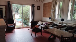 A living room with a sofa, chairs, a wooden table, and a view of the outdoors through large windows. - Large garden, private pool 5*9 m, 7 bedrooms, 3 bathrooms, 10 min walk to town center (Sanary-sur-Mer)