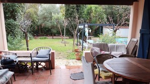 A covered patio with outdoor furniture, a swing set, and a view of a garden with trees and a white building. - Large garden, private pool 5*9 m, 7 bedrooms, 3 bathrooms, 10 min walk to town center (Sanary-sur-Mer)