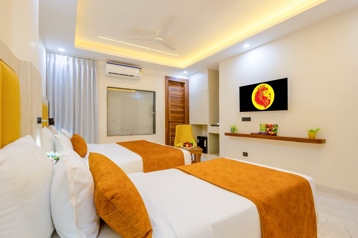 A hotel room with two beds, a television, a window, and a wall-mounted shelf with snacks.